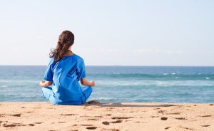 Female nurse meditating on a beach.