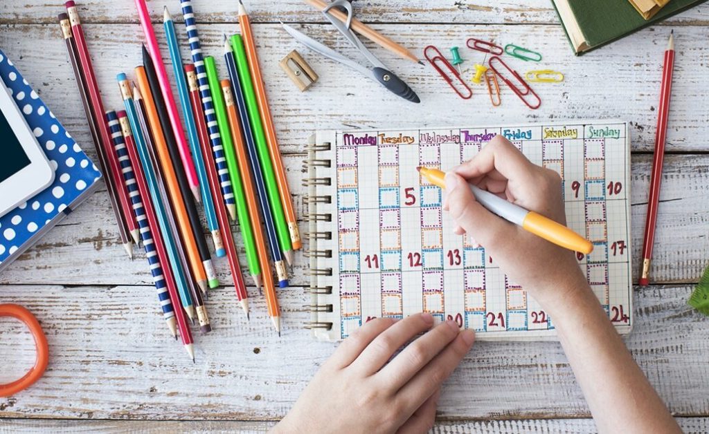 A teacher or student planning in a calendar with school supplies around.