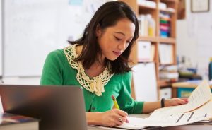 Female teacher working at a desk with papers and a laptop.