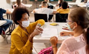 A teacher wearing a face mask appears to be reviewing a test with a student who is also masked.