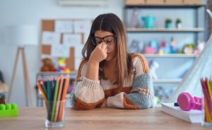 A female teacher with glasses looks stressed at a desk.