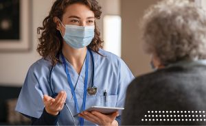 Nurse wearing a mask talking to an elderly patient.