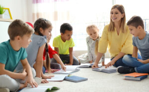 Female teacher working with students while sitting on the ground, reading books.