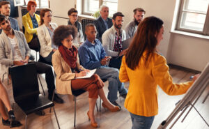 Female teacher instructing adult students in a classroom.